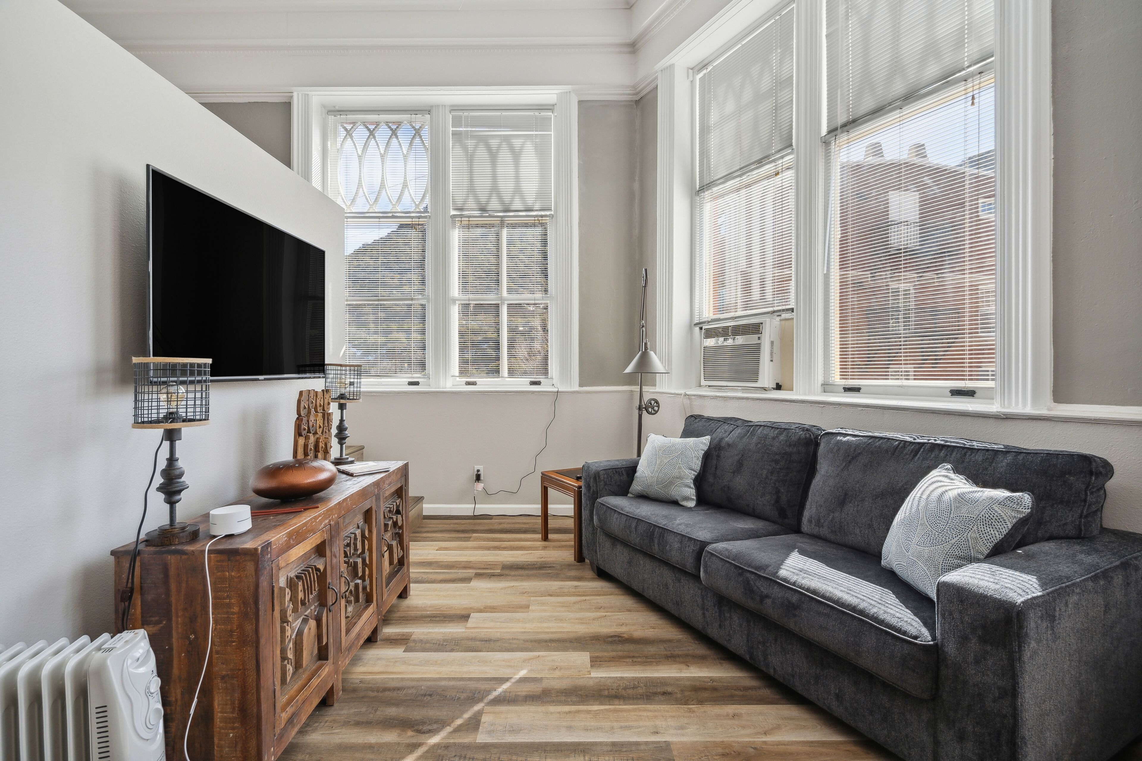 A living room with a grey sofa, wooden cabinet, and a flat-screen TV mounted on the wall.