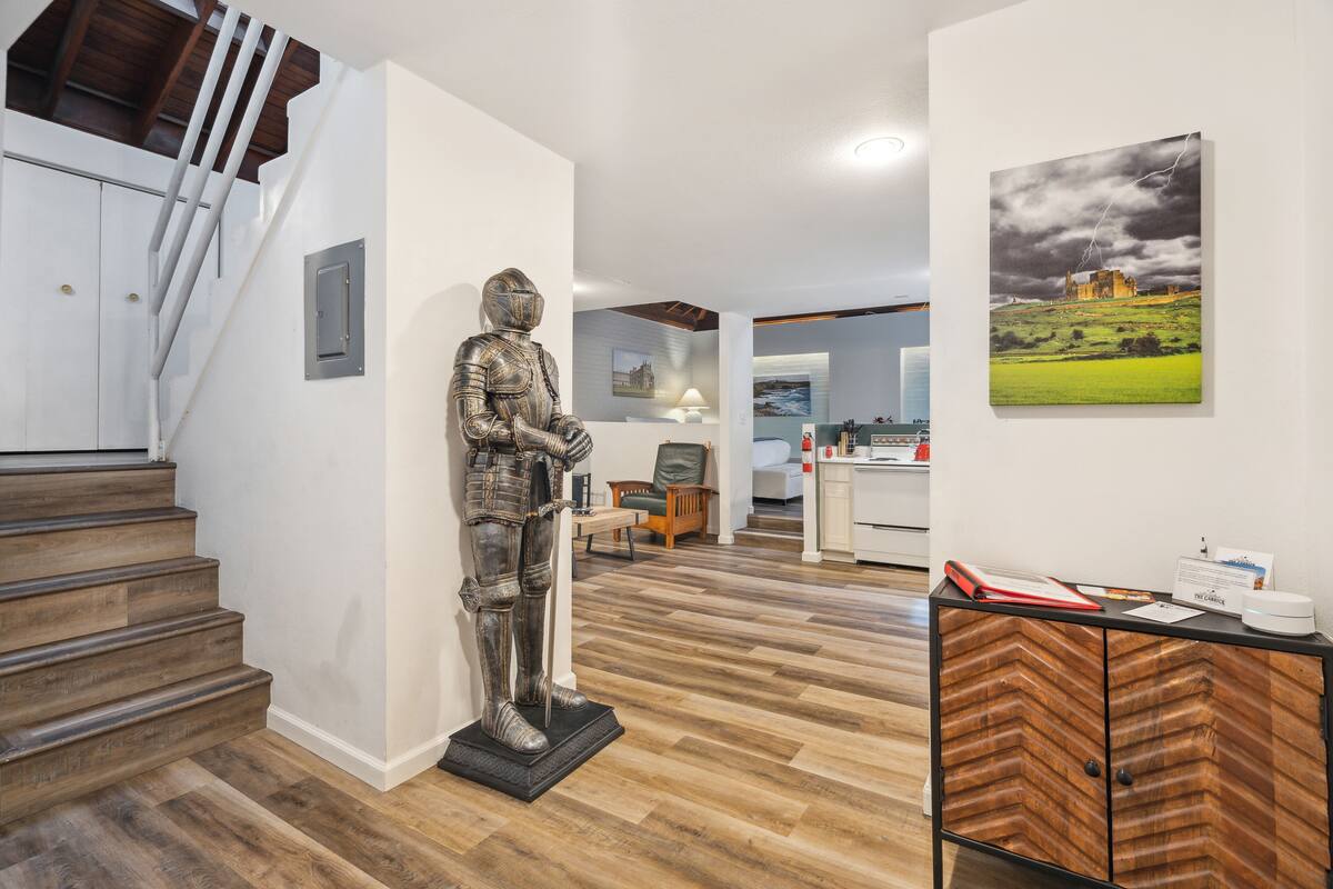 A modern interior with a wooden staircase, a statue, a wooden cabinet, and a painting of a castle.