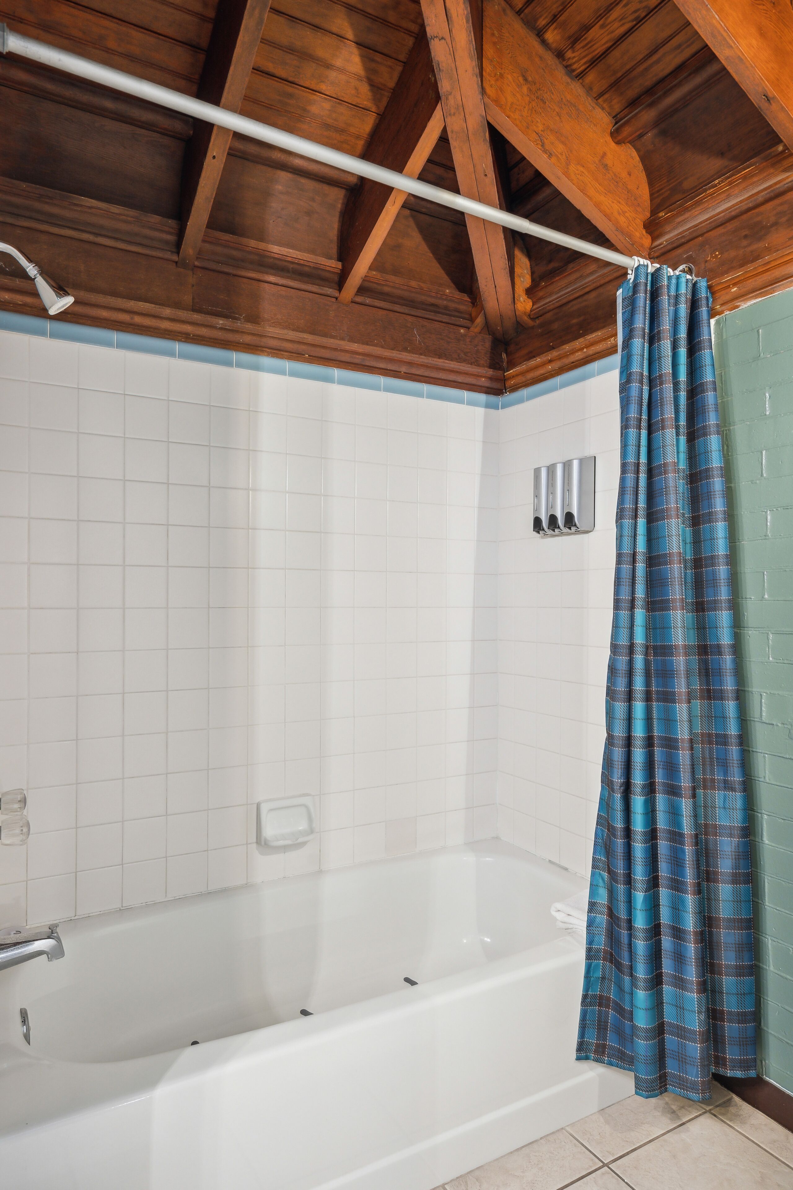 A bathroom with a white bathtub, a blue plaid shower curtain, and a wooden ceiling.