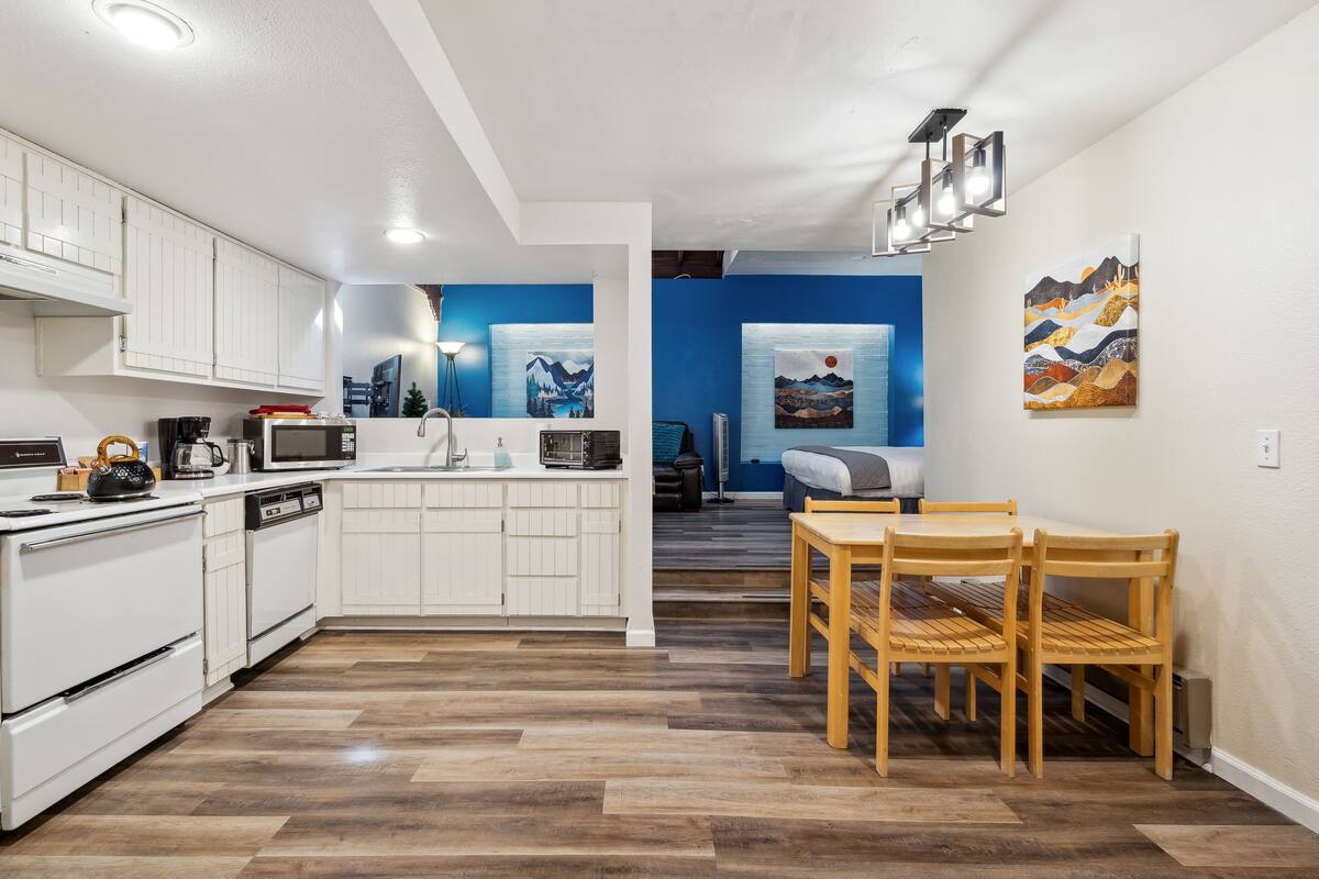 A modern kitchen with white cabinets, a dining area with wooden chairs, and artwork on the walls.