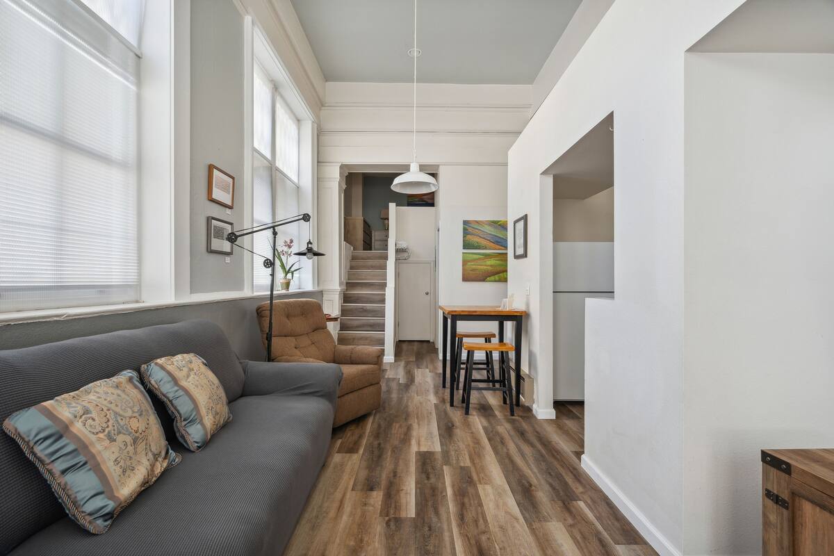 A modern living room with a gray sofa, wooden flooring, and a staircase leading to another room.