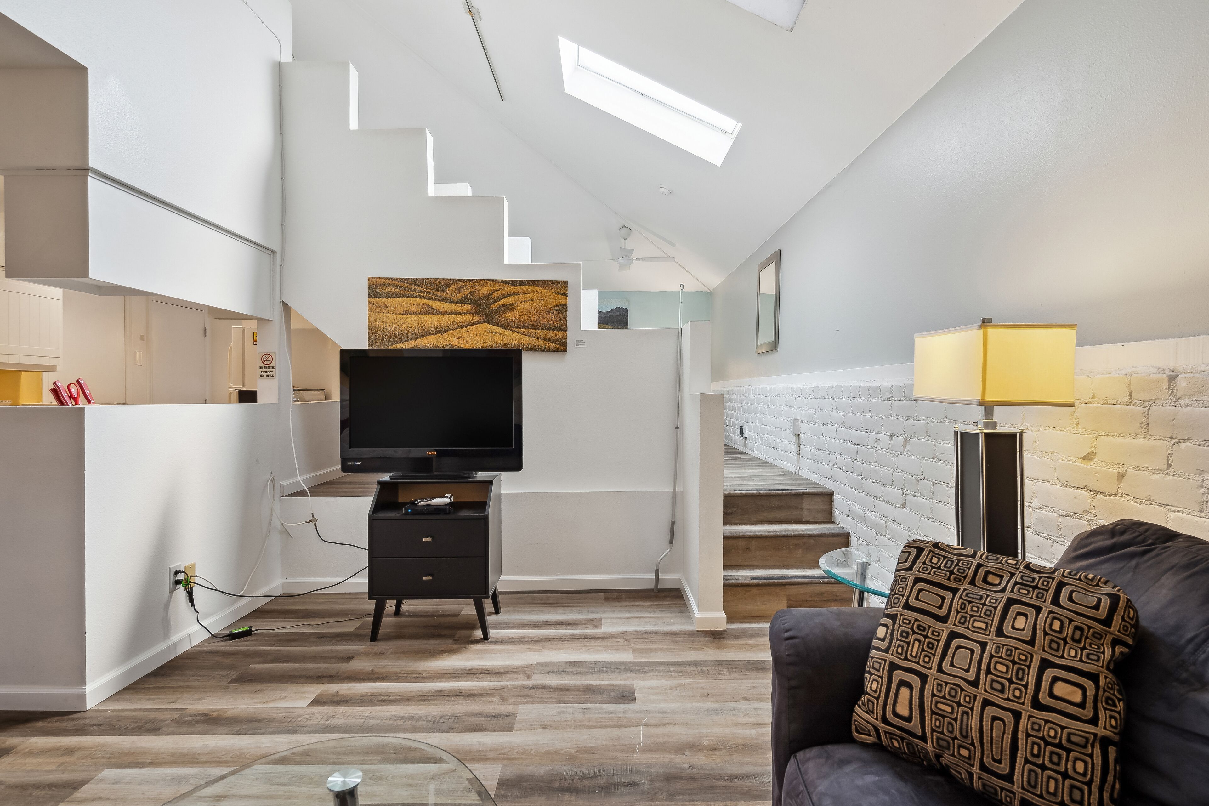 Uma sala de estar moderna com televisão de tela plana, almofada decorativa estampada, luminária e escada que leva a um andar superior.