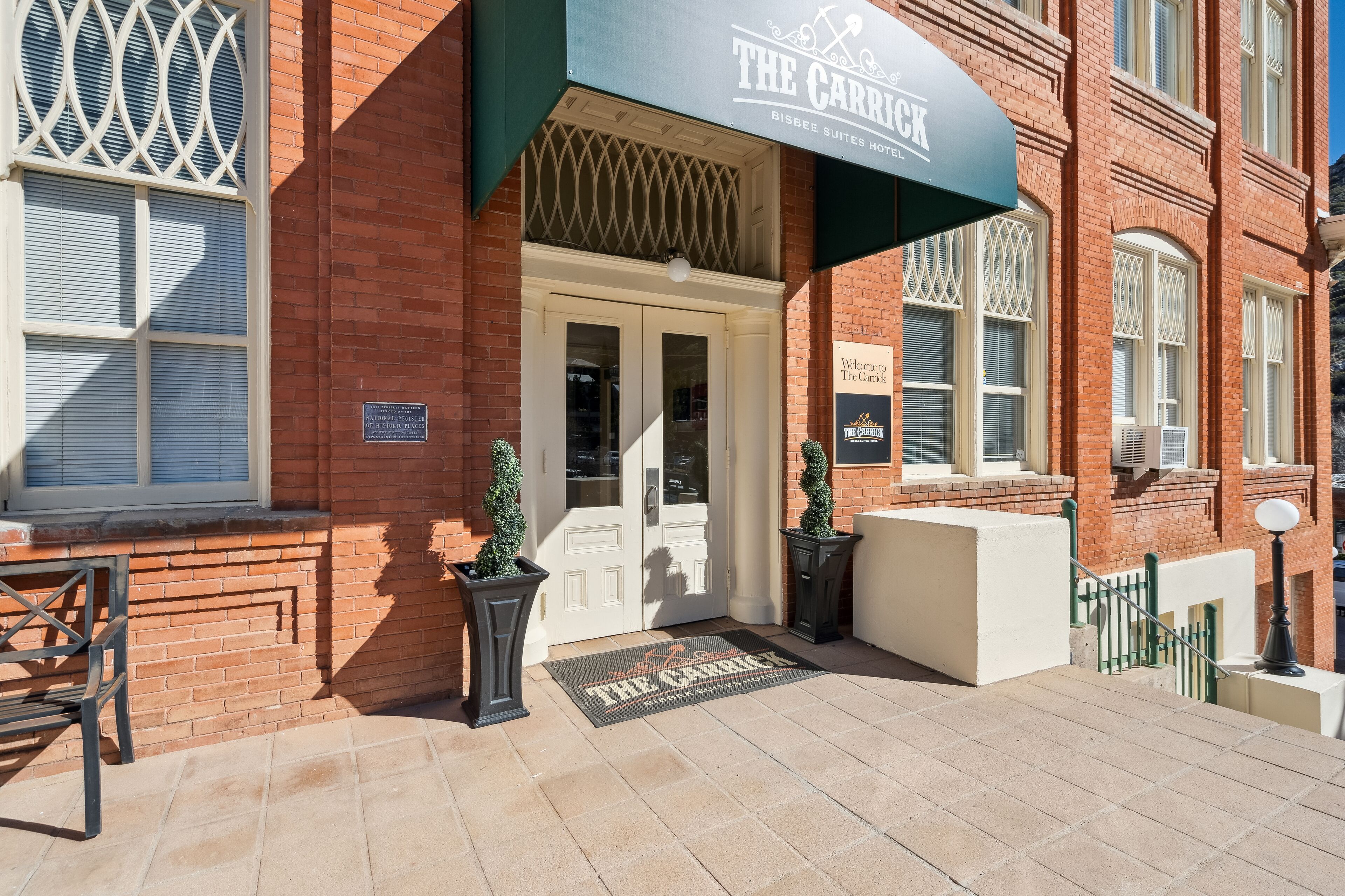 A hotel entrance with a sign reading "The Carrick," a brick facade, and a doormat with the hotel's name.