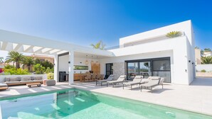 Una casa moderna con piscina, mobiliario exterior y zona de cocina.