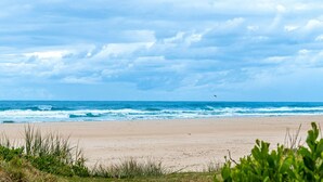 A beach with waves, a clear sky, and some vegetation in the foreground. - Beach Break - Embrace the coastal lifestyle, with a view that will steal your breath away (East Ballina)