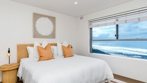 A bedroom with a large bed, a headboard, a bedside table with a lamp, a framed artwork above the bed, and a window with a view of the ocean. - Beach Break - Embrace the coastal lifestyle, with a view that will steal your breath away (East Ballina)