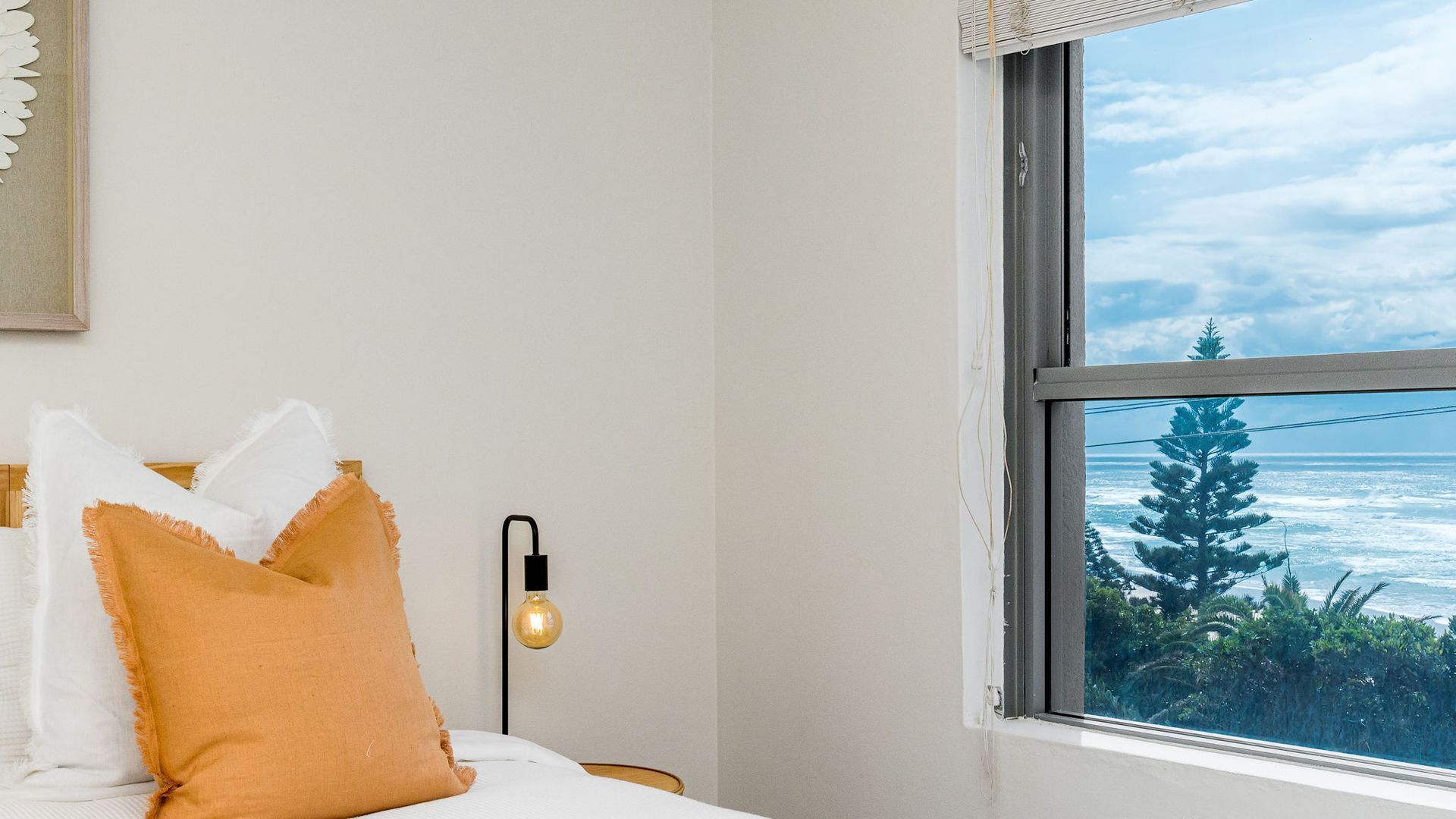 Une chambre avec un lit, une fenêtre donnant sur l’océan et un luminaire fixé au mur.
