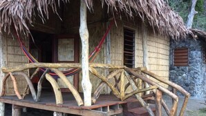A rustic wooden structure with a thatched roof, a wooden porch with a handrail, and a stone wall in the background.