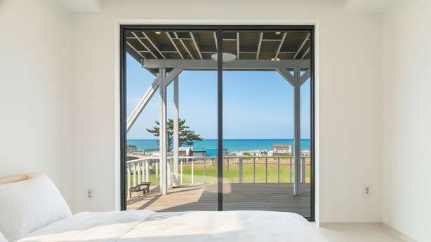 Ein Schlafzimmer mit einer großen Glasschiebetür, die auf einen Balkon mit Meerblick führt.