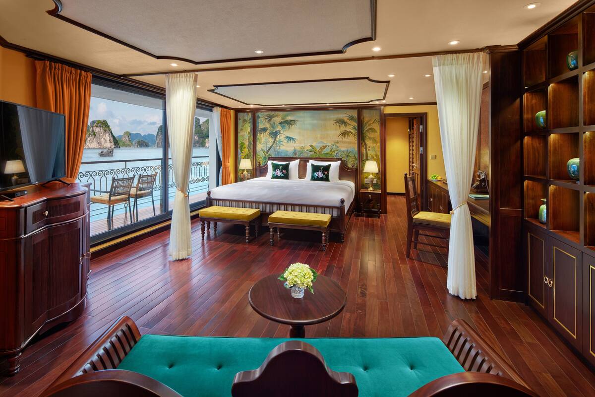 Ruime slaapkamer met groot bed, houten vloer, balkon met uitzicht op zee, en een zithoek met tafel en stoelen.