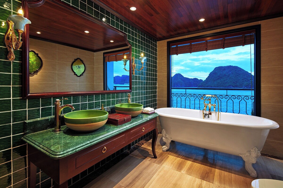 Ein Badezimmer mit einer freistehenden Badewanne, einem großen Spiegel und Blick auf eine gebirgige Landschaft durch ein Fenster.