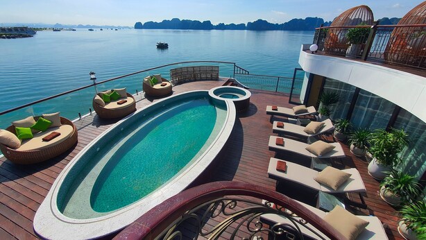 A pool area with lounge chairs and a hot tub, overlooking a body of water with boats and distant islands. - Indochine Premium Halong Bay (Tuan Chau)