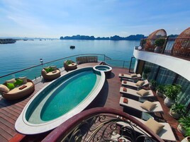 Zona de piscina con sillones reclinables y una bañera de hidromasaje, con vistas a una masa de agua con barcos e islas a lo lejos.