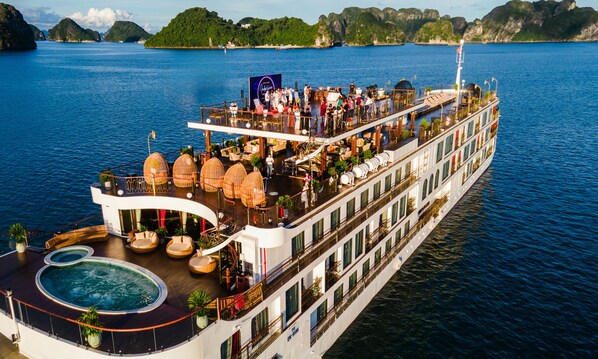 A large cruise ship with multiple decks, outdoor seating areas, and a pool.