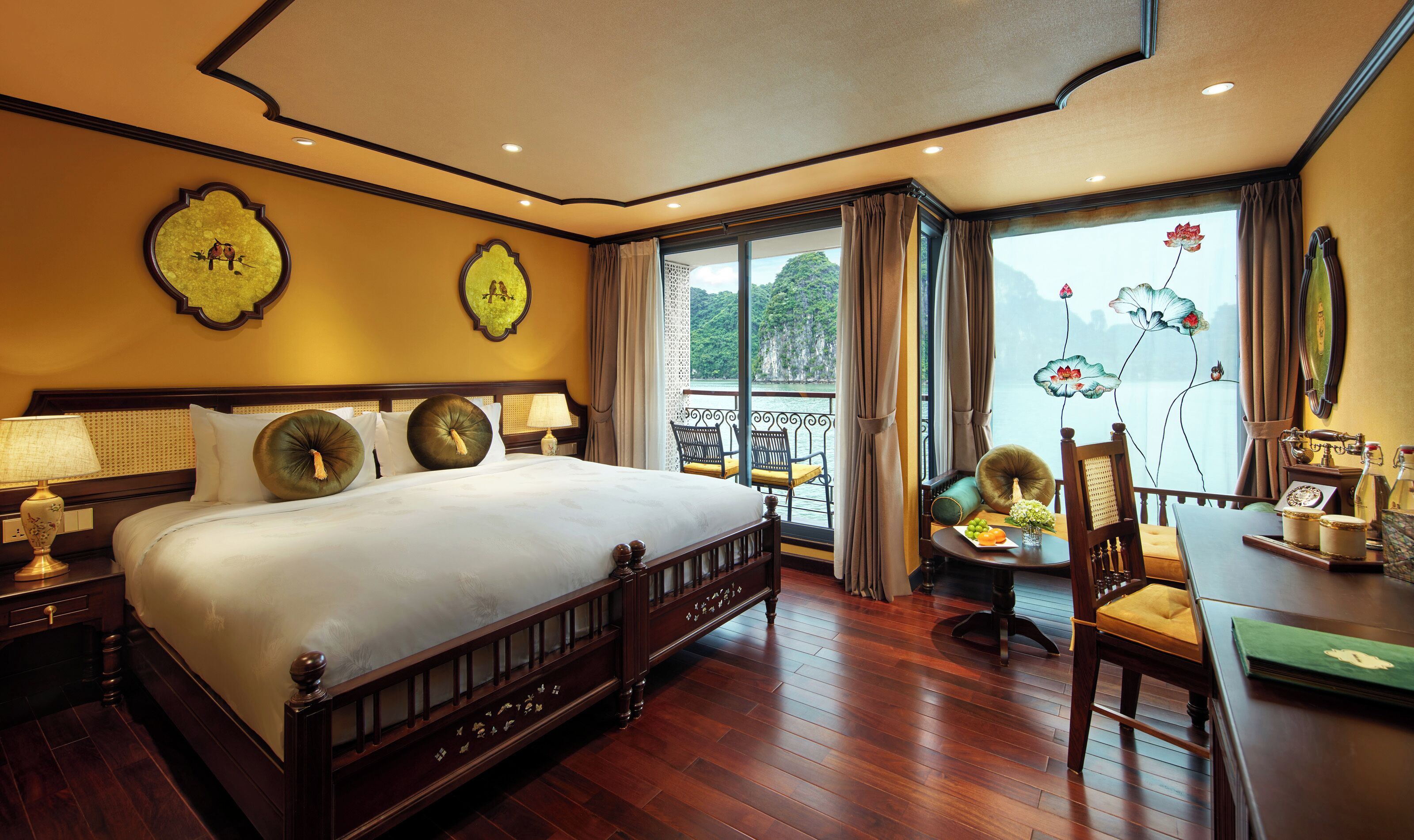 A hotel room with a large bed, a balcony with a view of the sea, and a dining area with a table and chairs.