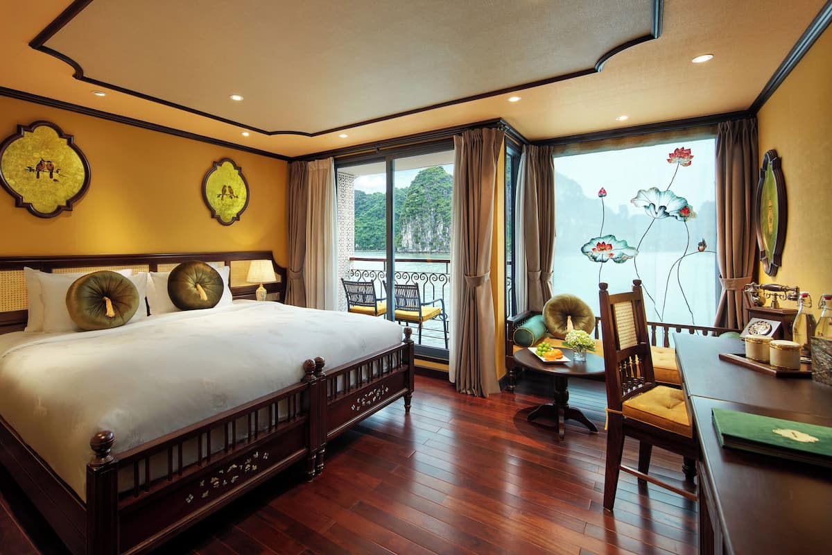 Een hotelkamer met een groot bed, een balkon met uitzicht op zee en een zithoek met een tafel en stoelen.
