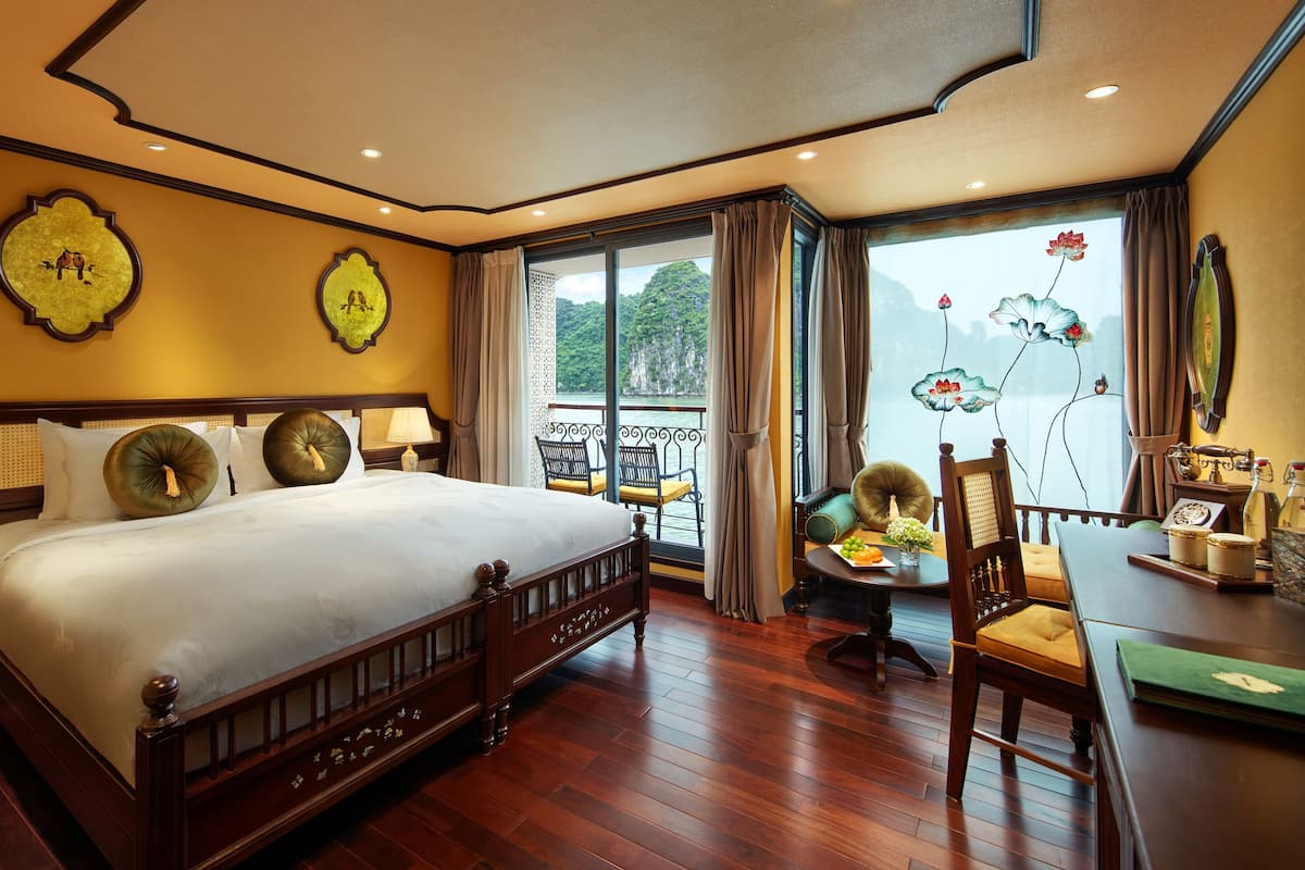 Een hotelkamer met een groot bed, een balkon met uitzicht op zee en een zithoek met een tafel en stoelen.
