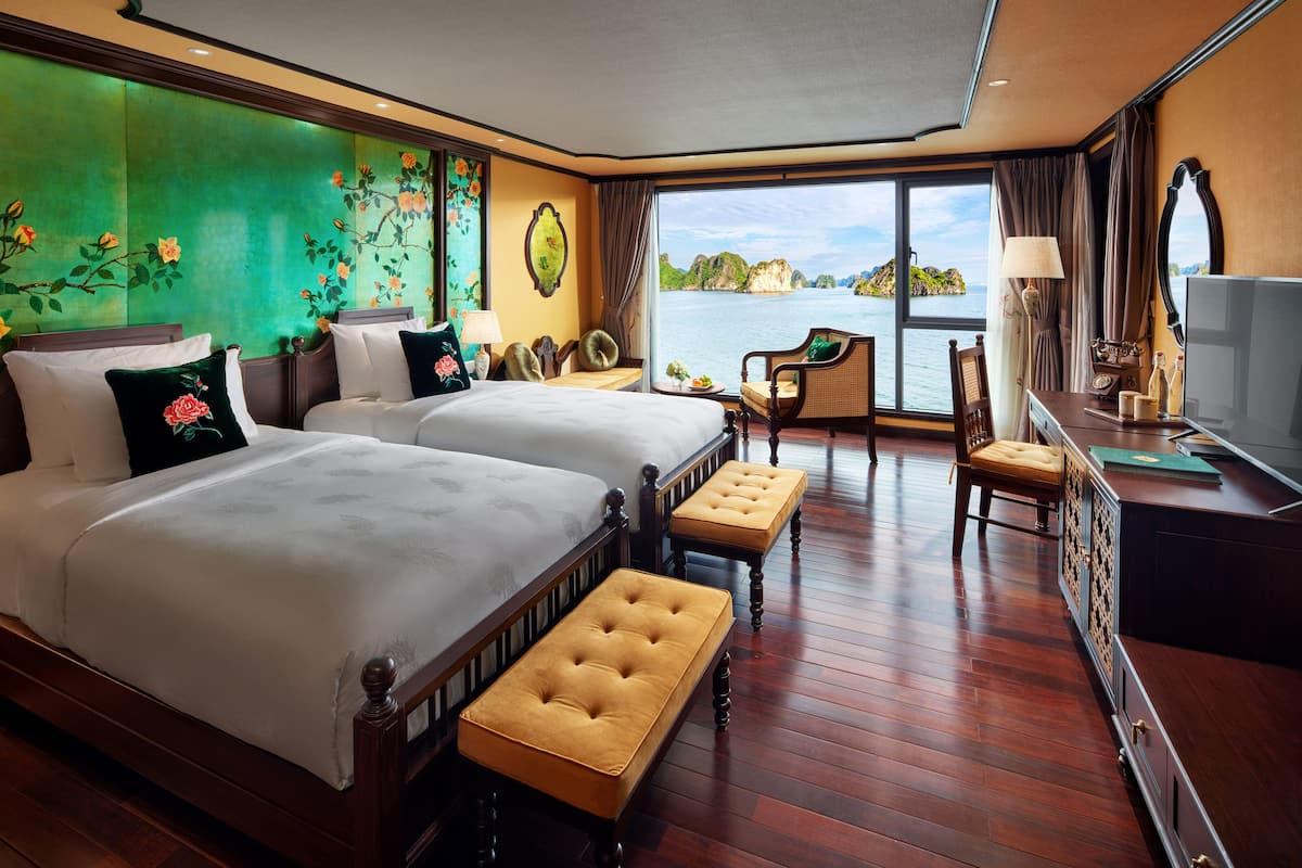 Een hotelkamer met twee bedden, een balkon met uitzicht op zee en een bureau met een televisie.