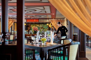 Un restaurante con mesas dispuestas para comer, un camarero atendiendo a una mesa y un techo decorativo.