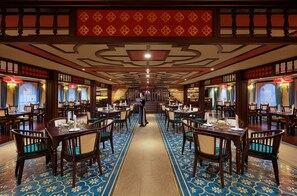 A hotel lobby with a central walkway, tables, chairs, and a decorative ceiling.
