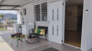 Una habitación limpia y moderna con un ventanal grande, una puerta con un letrero decorativo, una mesita con cuencos y un banco con cojines.