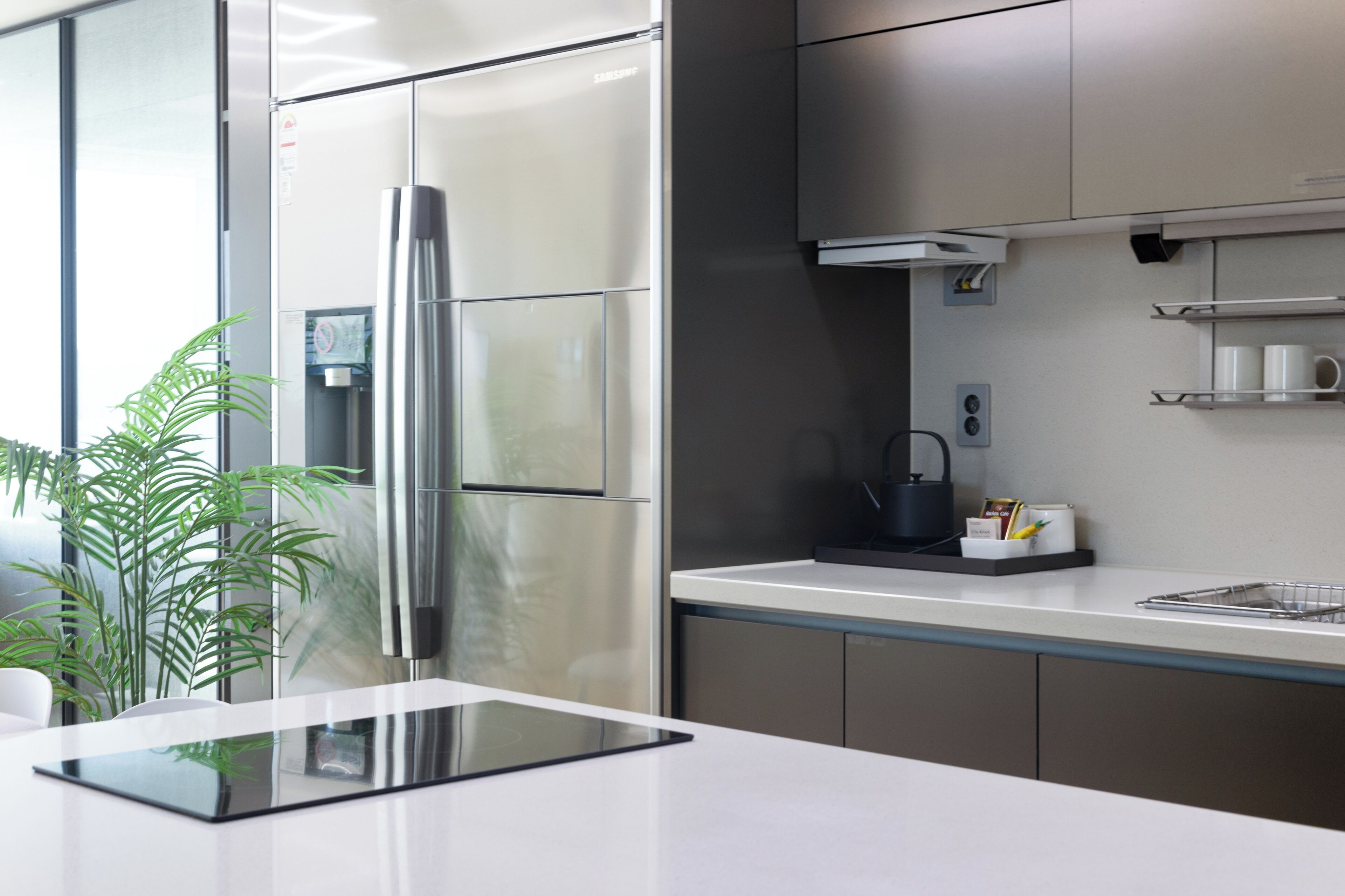 Een moderne keuken met roestvrijstalen apparatuur, een wit aanrecht en een kleine plant.