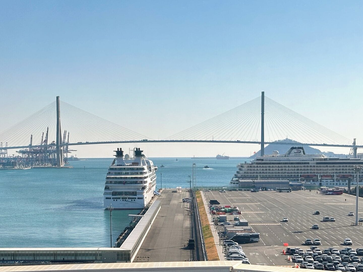 A cruise ship docked at a port with a large bridge in the background.