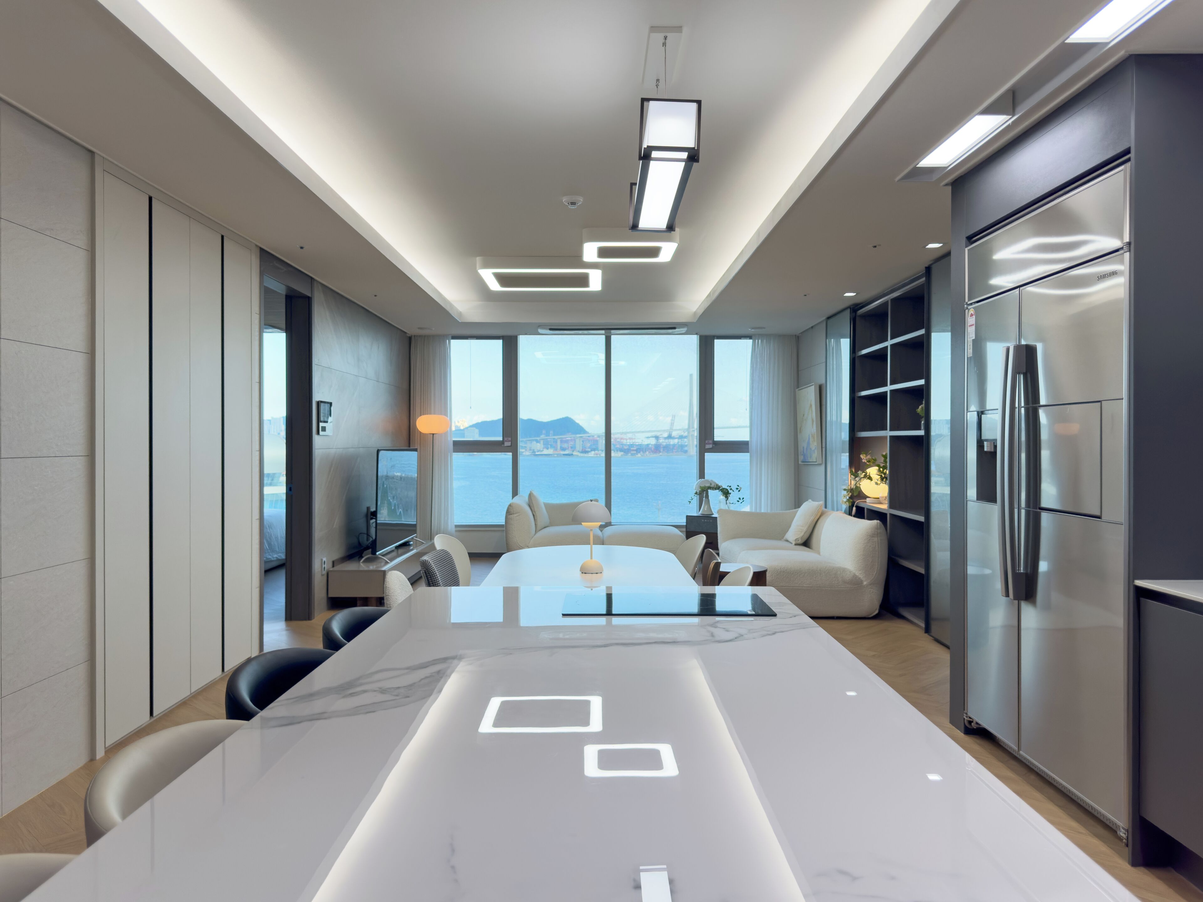 A modern kitchen with a large island, built-in appliances, and a view of the sea.