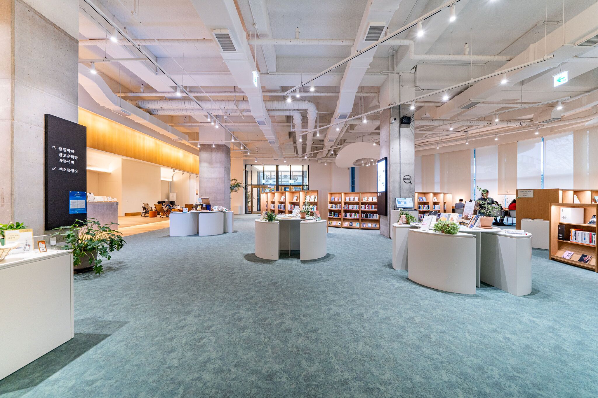 Una biblioteca amplia con varias zonas de lectura, estanterías y una mesa central para exhibiciones.