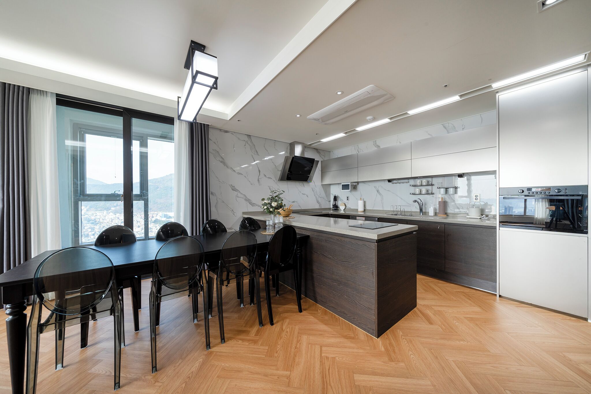 Una cocina moderna con una isla grande, piso de madera oscura y vistas de la ciudad a través de amplios ventanales.