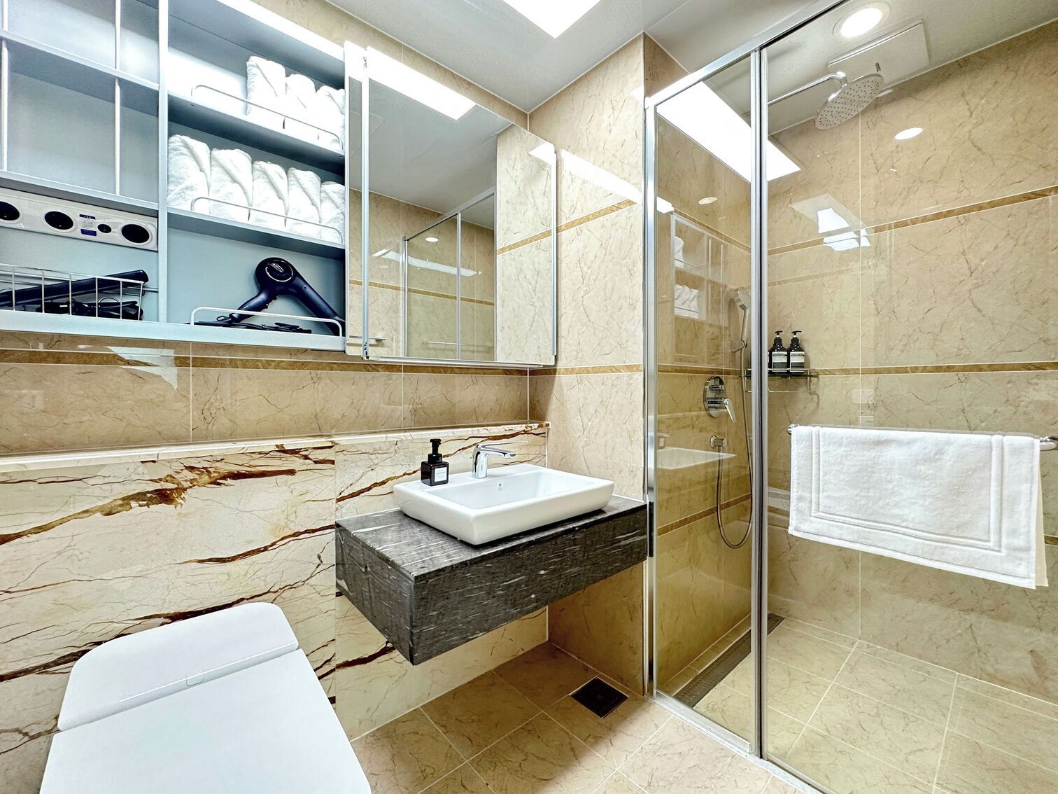 A modern bathroom with a glass-enclosed shower, a white sink, and a marble-tiled wall.