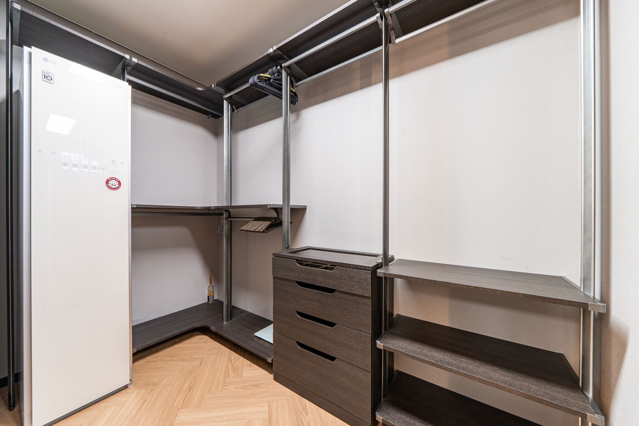 A compact, modern closet with built-in shelves and drawers, featuring a minimalist design and a herringbone-patterned floor.