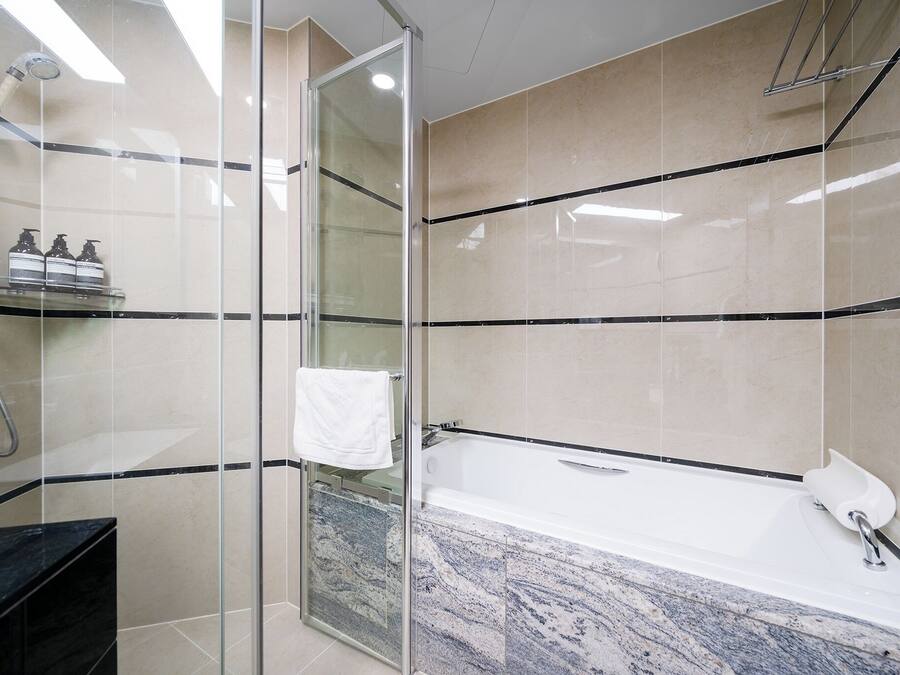 A modern bathroom with a glass-enclosed shower, a marble sink, and a bathtub.