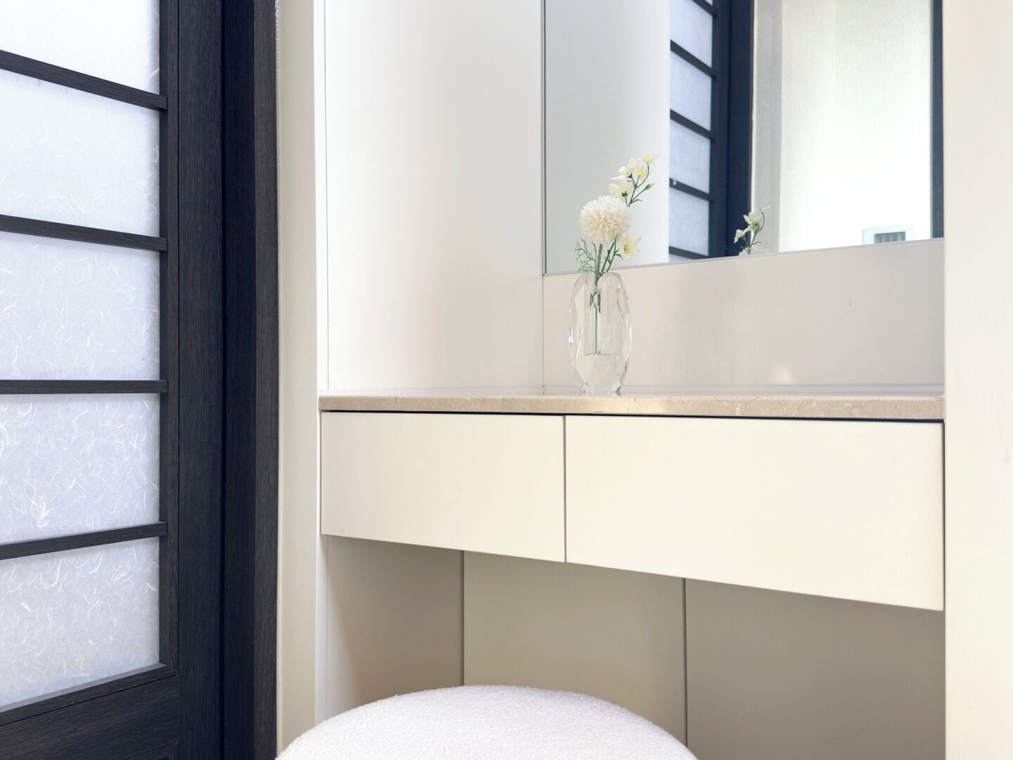 Un baño con tocador blanco, espejo y un florero con flores.