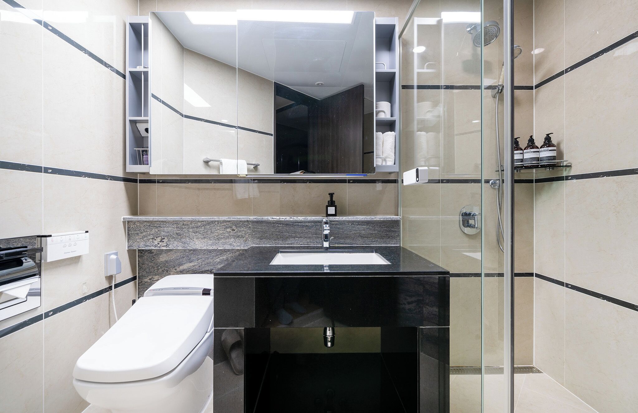 A modern bathroom with a glass shower enclosure, a white toilet, and a black sink with a mirror above.