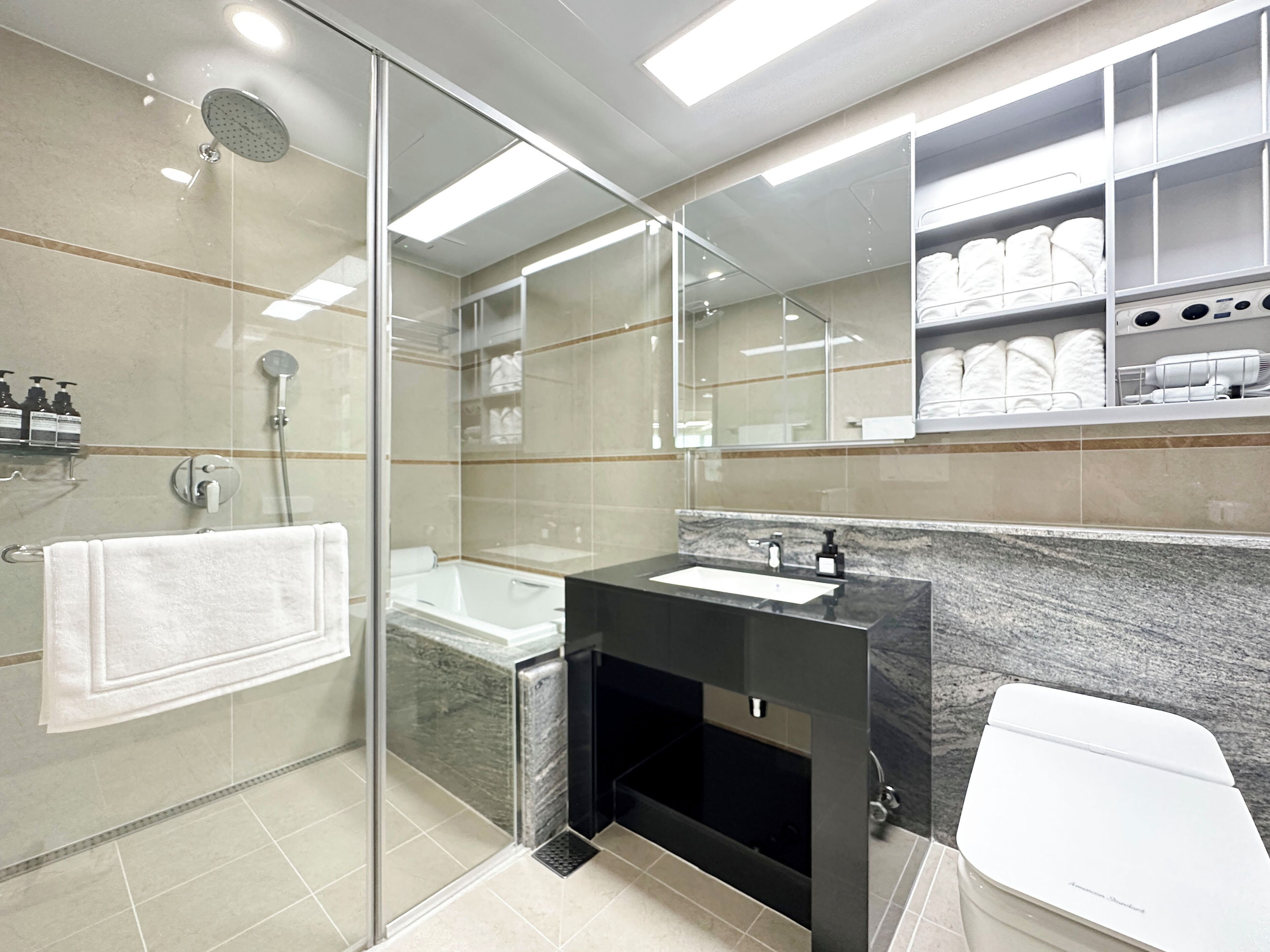 A modern bathroom with a glass-enclosed shower, a bathtub, a vanity with a sink, and a toilet.