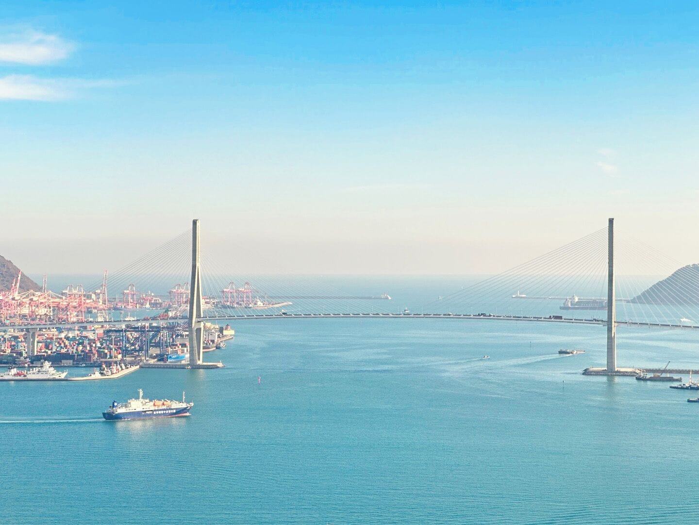 Un maestoso ponte sospeso che si estende su un tratto d'acqua, con un porto e uno skyline urbano sullo sfondo.