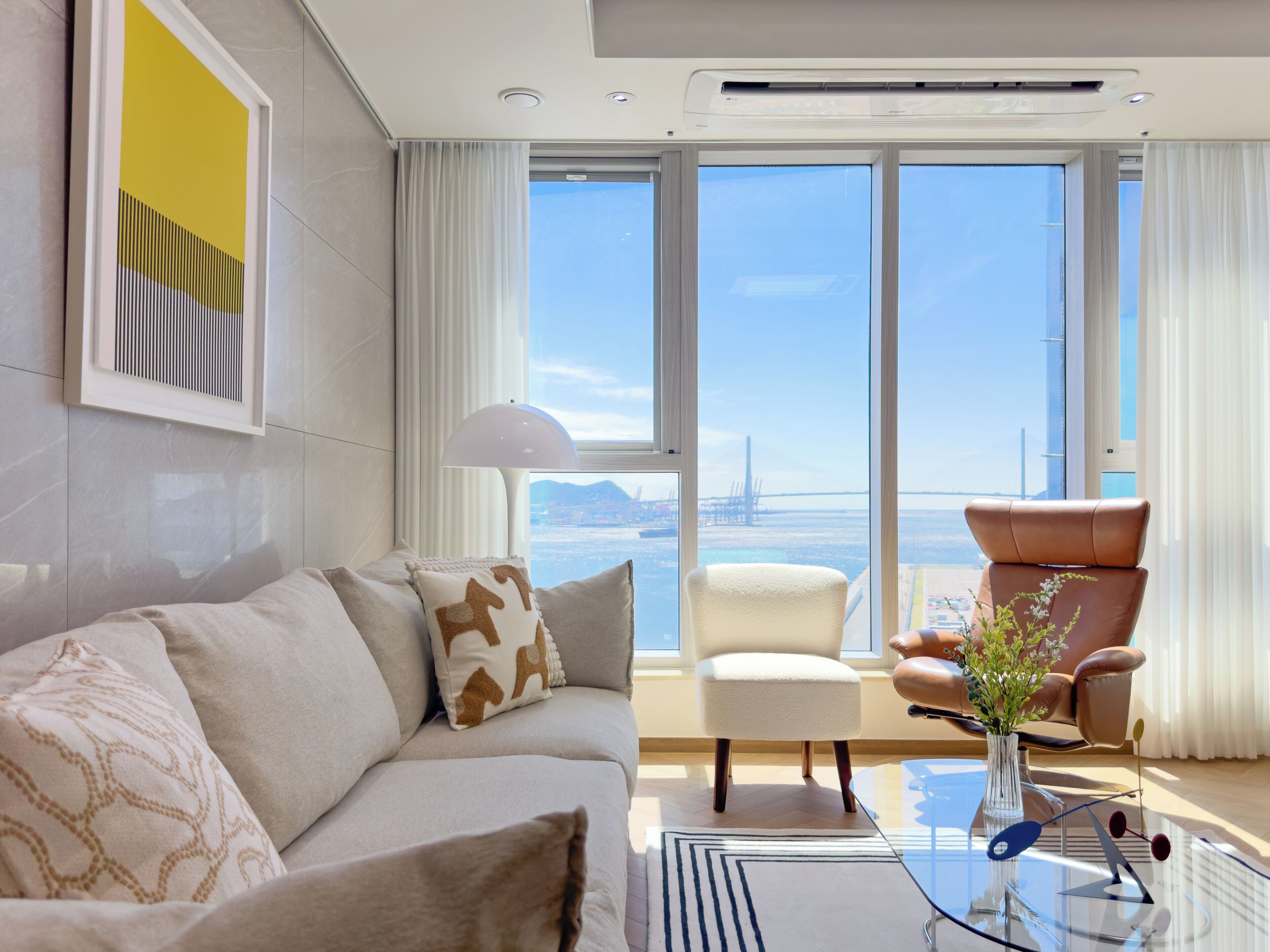 A modern living room with a sofa, armchairs, a coffee table, and a view of a bridge and water.