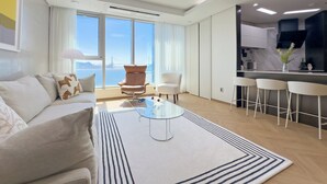 Una sala de estar moderna con un sofá, una mesa de centro de vidrio y vistas de la ciudad a través de amplios ventanales.