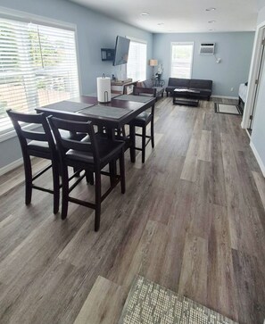 A spacious living area with a dining table and chairs, a sofa, and a television mounted on the wall. - Studio "Grande" (Lakeland)