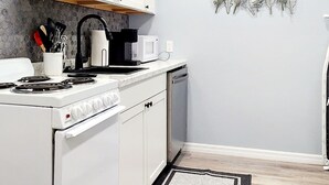 A modern kitchen with white cabinets, a stove, a microwave, and a coffee maker. - Studio "Grande" (Lakeland)