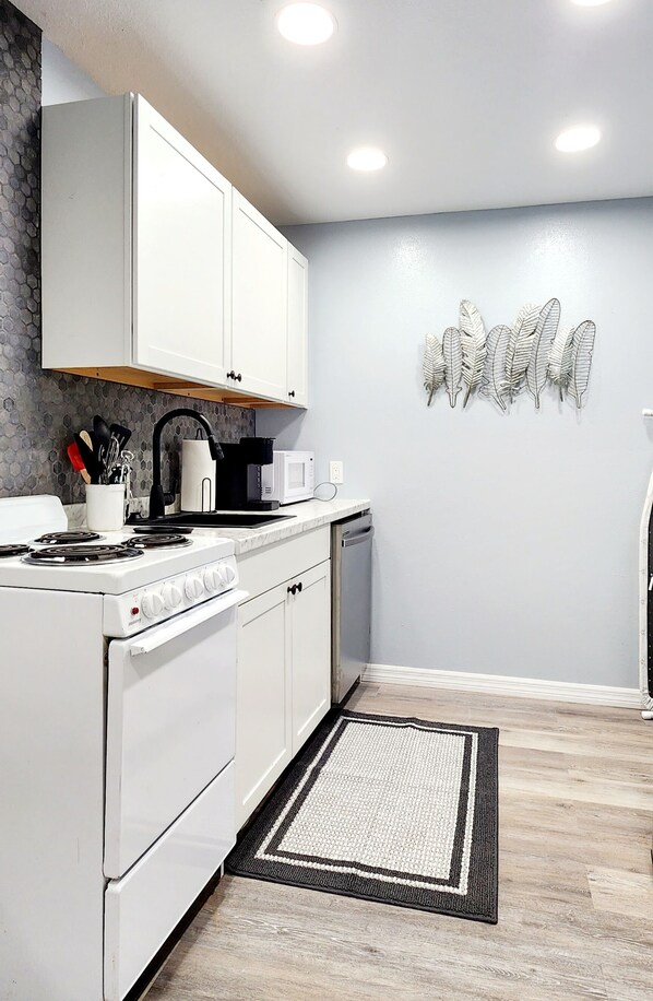 A modern kitchen with white cabinets, a stove, a microwave, and a coffee maker. - Studio "Grande" (Lakeland)