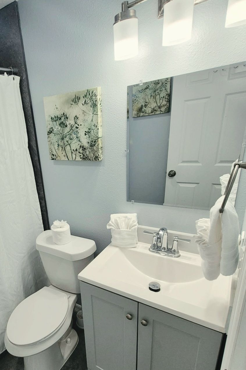 A bathroom with a toilet, sink, and mirror. There are towels on the sink and a shower curtain.