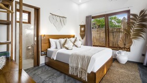 A bedroom with a wooden bed, a large window with a view of greenery, a wall-mounted clock, and a hanging decorative piece. - Villa Grateful by Alfred in Bali (Sukawati)