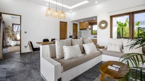 A modern living room with a sofa, coffee table, and hanging light fixtures. - Villa Grateful by Alfred in Bali (Sukawati)