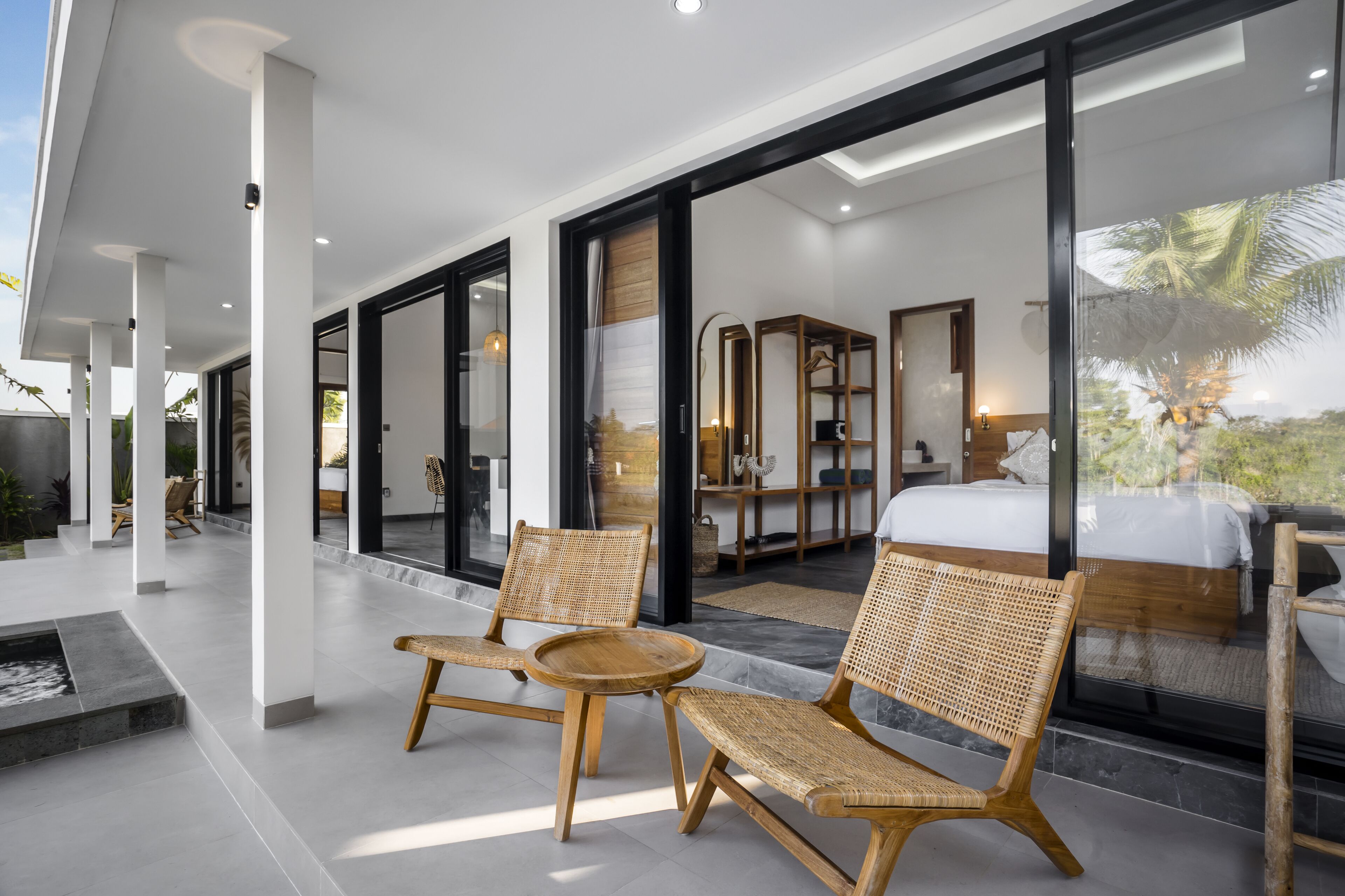 A modern hotel room with a large bed, a bathroom with a shower, and a balcony with wicker furniture.