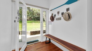 Habitación con banca de madera, puerta que da al exterior, sombreros y remo colgados en la pared.
