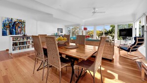 Un comedor amplio con una mesa de madera y sillas de mimbre, una estantería y un ventanal con vistas al exterior.