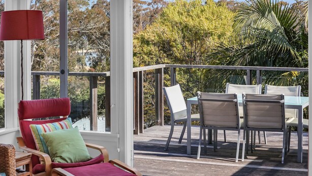 Una terraza con una silla roja, una mesa y dos sillas, con vista a árboles y una palmera.