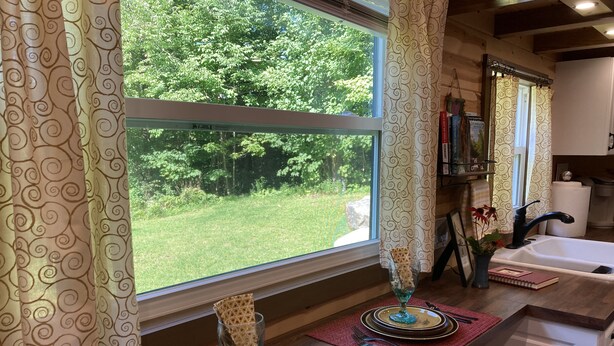A dining area with a view of a garden, a sink, and a mirror. - Charming Tiny House on 10 Wooded Acres (Richmond)